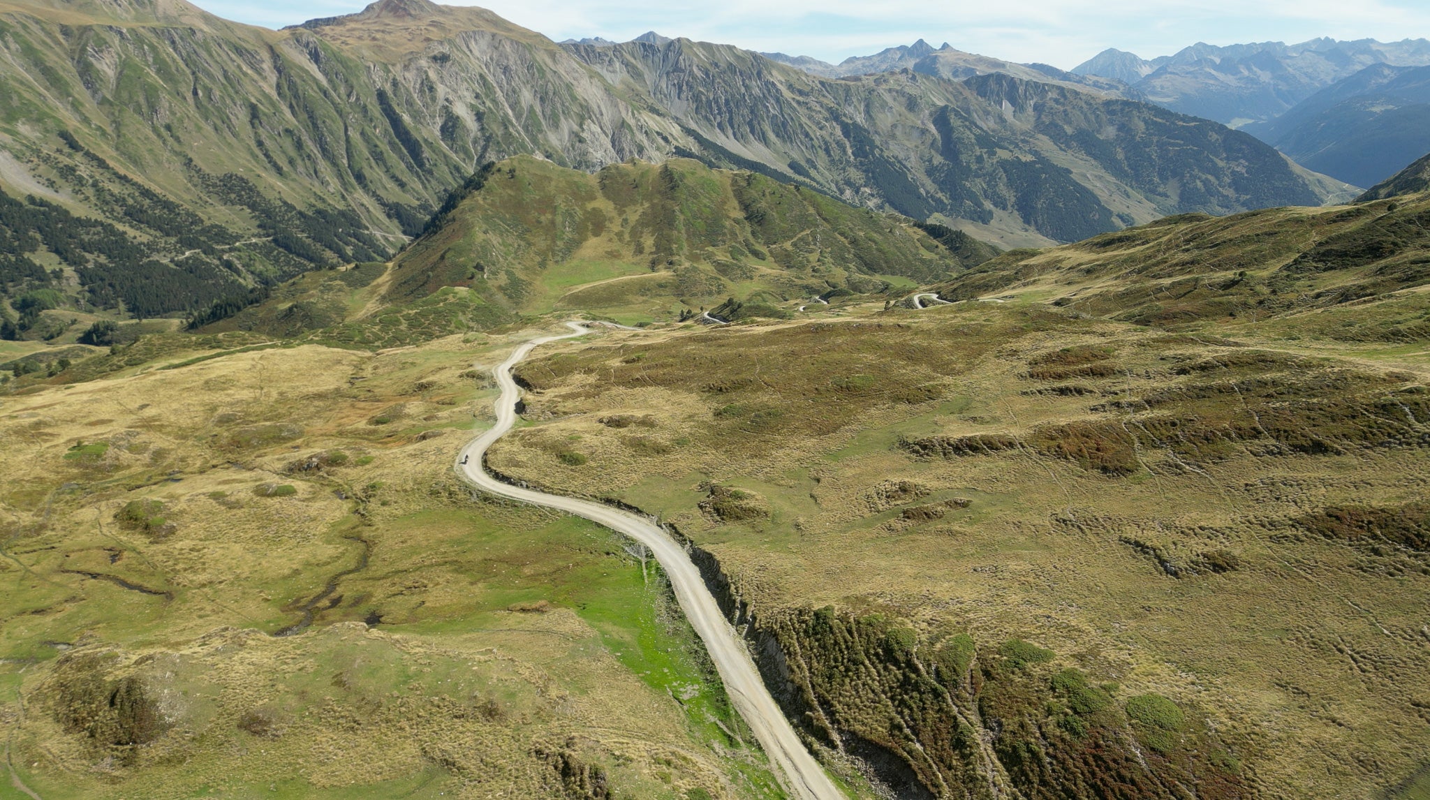 Winding road through a mountainous landscape with green hills and a clear sky.